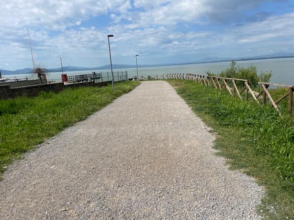 Schotterradweg am Eingang des Parks von Passignano, gesäumt von Gras und einem Zaun, der ihn vom See trennt.